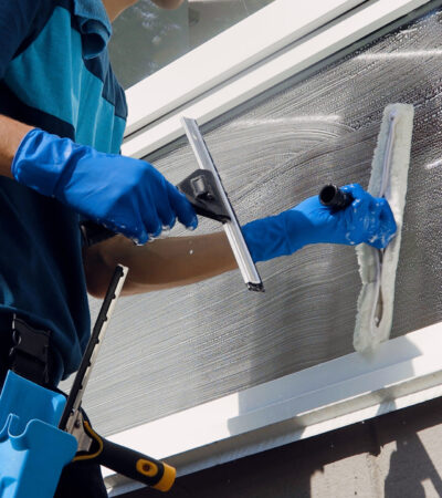 Male professional cleaning service worker in overalls cleans the windows and shop windows of a store with special equipment.