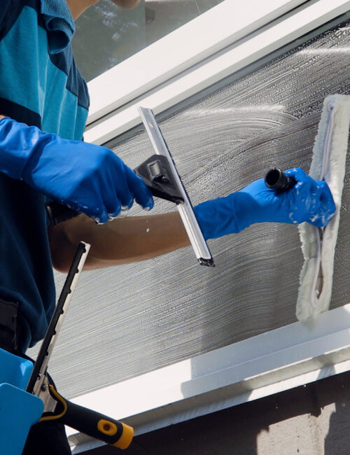 Male professional cleaning service worker in overalls cleans the windows and shop windows of a store with special equipment.